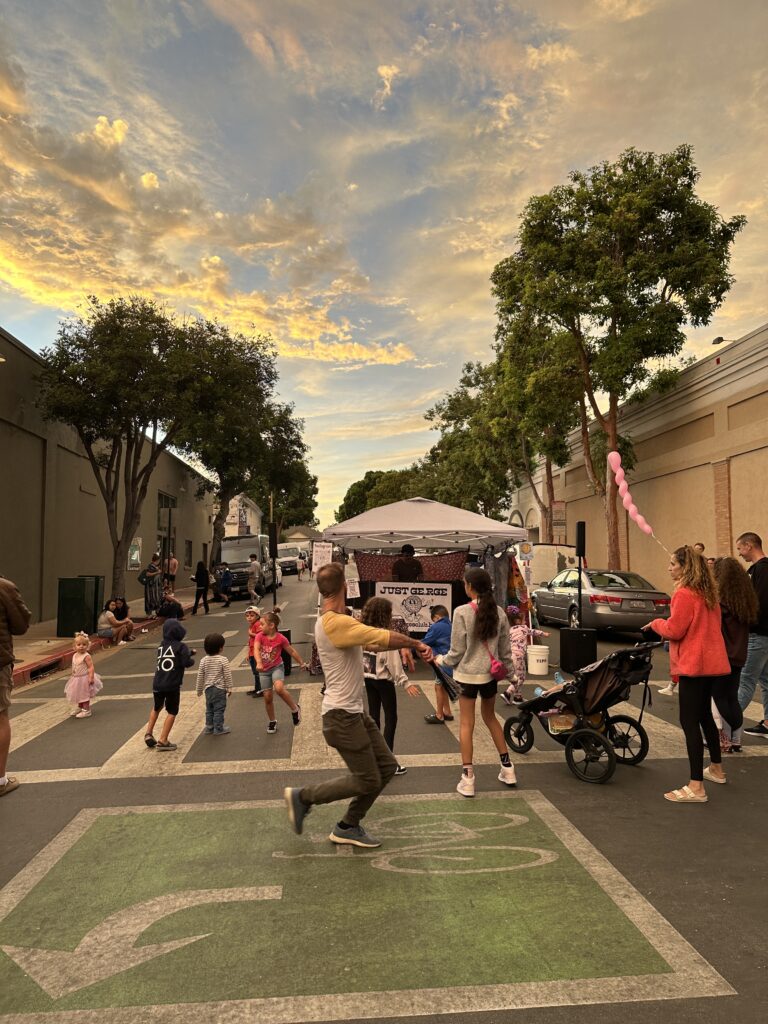 just ge.rge playing at the San Luis Obispo Farmers Market with a crowd dancing in the foreground and a beautiful sunset in the background